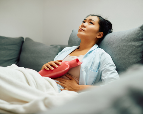 young woman holding hot water bottle on her stomach at home