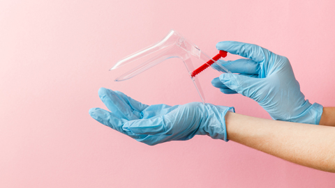 gynecological speculum in woman's hands in medical sterile gloves on pink background